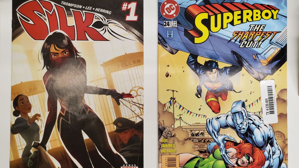 On the left a comic book cover shows a woman with black hair wearing a face mask and a black and red suit shooting webs from her left hand. On the right a comic cover shows Superboy lifting a car over a silver man with long sharp fingers who is holding a woman down.