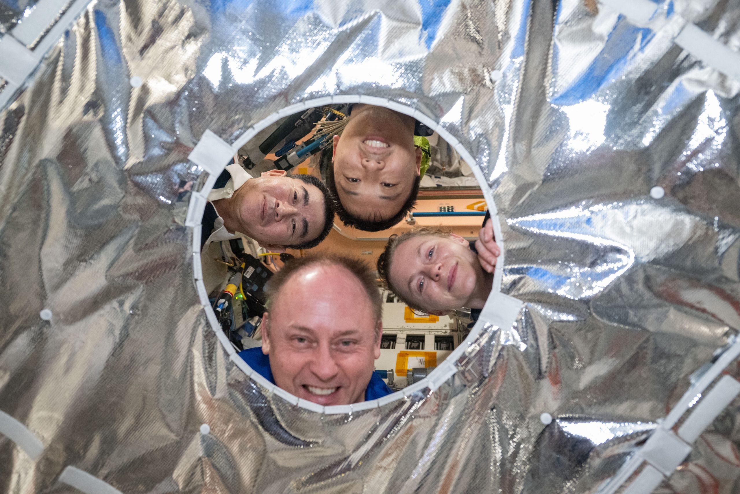 Peekaboo! – Clockwise from left, JAXA (Japan Aerospace Exploration Agency) astronaut Kimiya Yui and NASA astronauts Jonny Kim, Zena Cardman, and Mike Fincke pose for a playful portrait through a circular opening in a hatch thermal cover aboard the International Space Station on Sept. 18, 2025.