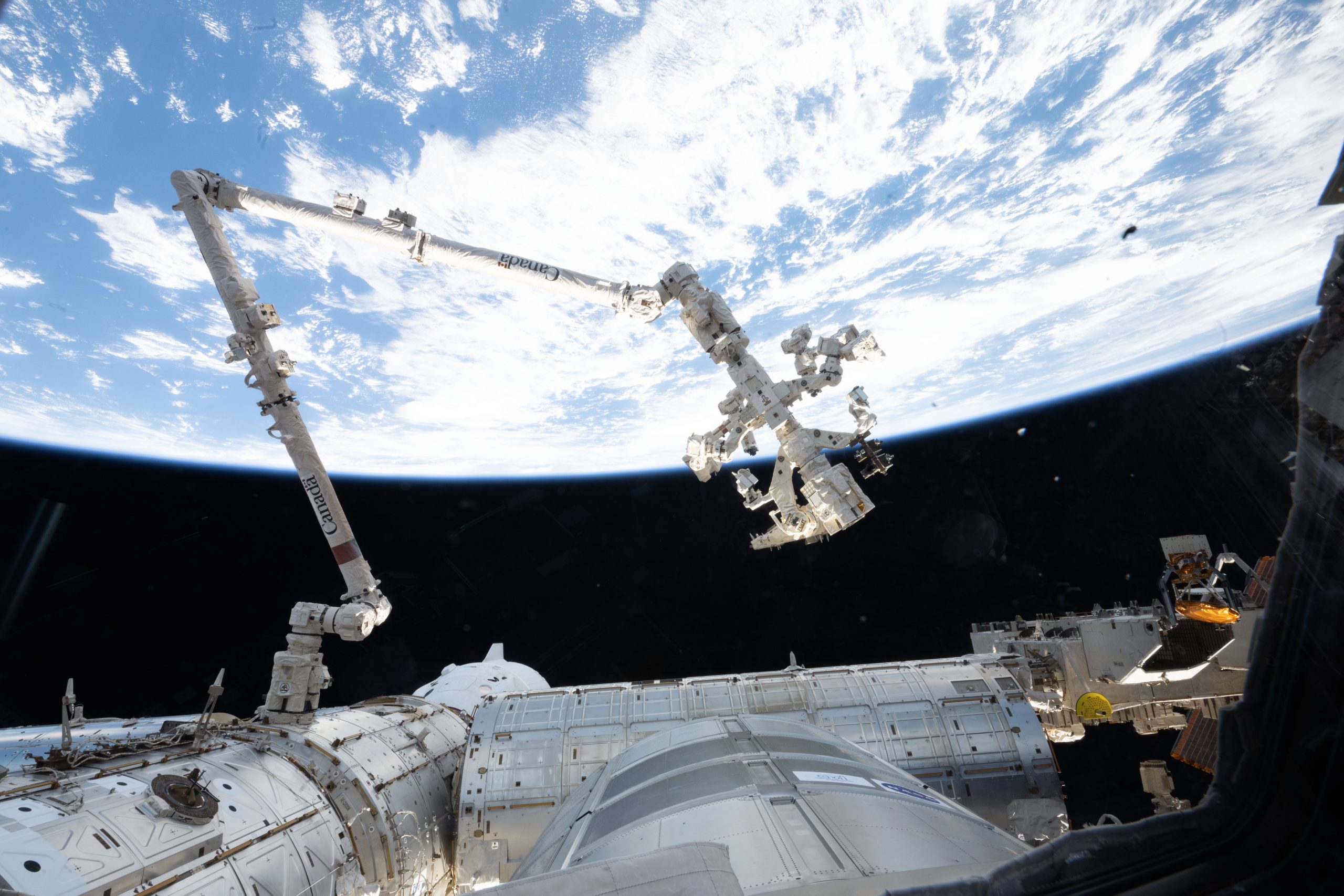 A Robotic Helping Hand – The 57.7-foot-long Canadarm2 robotic arm extends from a data grapple fixture on the International Space Station’s Harmony module in this July 23, 2025, image.