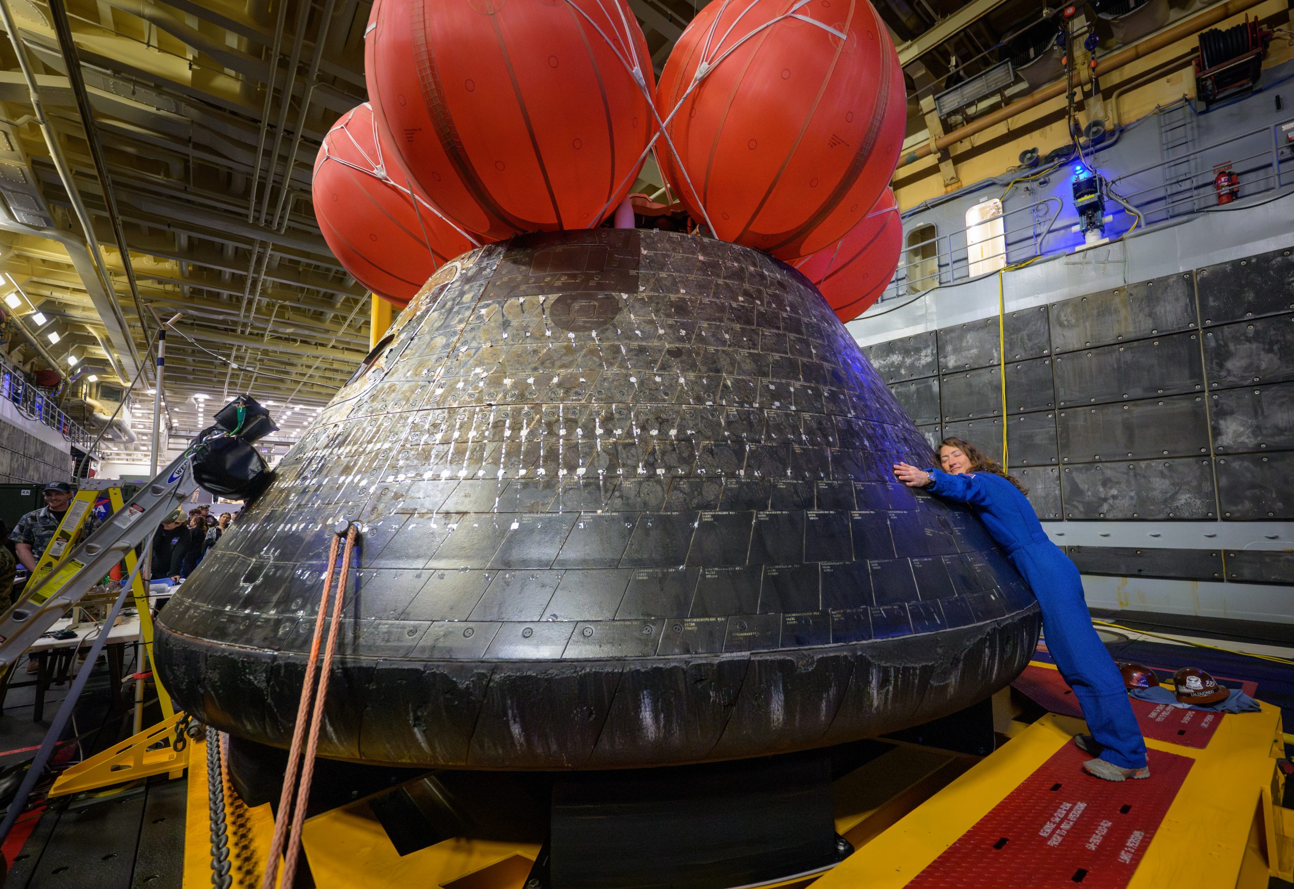 A Hug for Home Away from Home – NASA astronaut Christina Koch, Artemis II mission specialist hugs the Orion spacecraft in the well deck of USS John P. Murtha, Saturday, April 11, 2026.