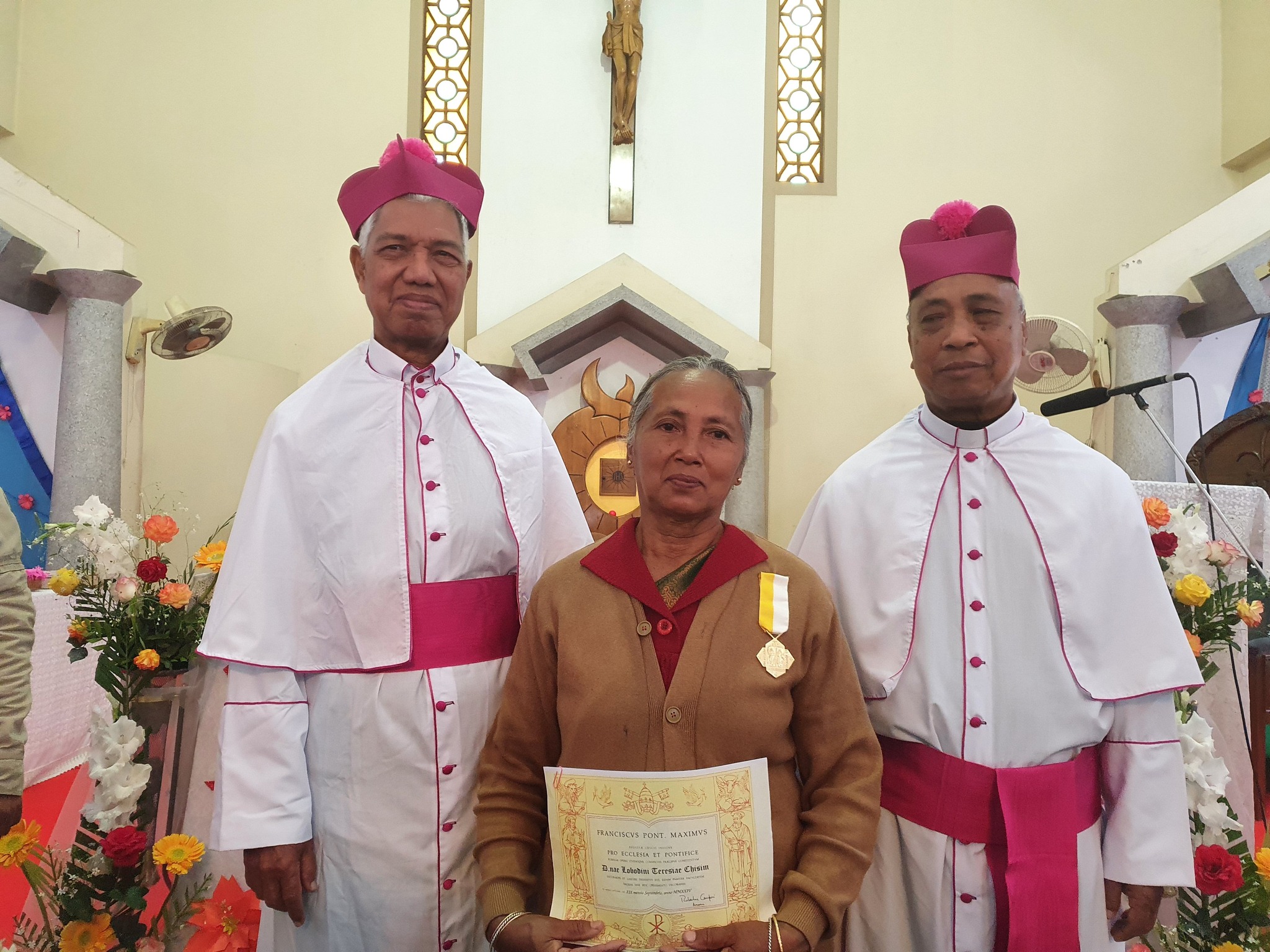 The laywoman who has quietly formed a generation of priests and sisters in South Asia – #Catholic – MYMENSINGH, Bangladesh — In a country where Catholic vocations often emerge from modest rural communities, the quiet influence of lay Catholics can be decisive. For decades, Lobdine Chisim, a lay teacher and catechist from Mariamnagar Parish in Bangladesh’s Diocese of Mymensingh, has been one such influence — helping shape a generation of priests and religious sisters through personal sacrifice, faithful accompaniment, and maternal care.Chisim, 65, received the papal honor “Pro Ecclesia et Pontifice” in 2025 in recognition of her lifelong service to the Church. The award highlighted a vocation lived not in vows or ordination but in persistent support of Catholics discerning consecrated life.Mariamnagar Parish, founded in 1937 by American Holy Cross missionaries, has produced at least eight priests and seven religious sisters over the years. According to clergy and religious from the parish, Chisim has played a role — both direct or indirect — in nearly all of those vocations.
 
 Lobdine Chisim at her home in Mariamnagar Parish on April 24, 2026. | Credit: Photo courtesy of Lobdine Chisim
 
 A member of the parish, Chisim teaches at the local Catholic school and serves as a catechist. Known for her fidelity to Church teaching and firm moral guidance, she has long accompanied young people considering the priesthood or religious life, often stepping into roles usually filled by parents or formal formation staff.Though never officially assigned to a seminary or formation house, Chisim has acted quietly and become what local clergy call a “caregiver of vocations,” introducing boys and girls to seminaries and religious congregations, helping them navigate formation, and supporting them materially when poverty threatened to derail their calling.Chisim, the mother of one child, personally financed the seminary education of her younger brother — now Father Joseph Chisim. Beyond her family, she has continued to follow the progress of seminarians and candidates, remaining in contact with them through letters, visits, and phone calls, particularly during moments of doubt or crisis.Father Sanchaya Ignatius Chisim (no relation to Lobdine Chisim), rector of St. Paul’s Minor Seminary in Jalchatra, Tangail, credits the influence of the laywoman as decisive in his own discernment. Speaking to EWTN News, he said she first inspired him while teaching catechism classes during his school years.“She encouraged me to enter the seminary and continued to guide me after I joined,” he said. “She gave me advice and counseling, and many times helped me financially while I was a seminarian.”During vacations home from the seminary, Father Chisim recalled, she would regularly check on him. “She protected me like a mother and warned me against temptation. She played an important role in my becoming a priest, and I am grateful to her.”Religious sisters from Mariamnagar Parish offer similar testimony.Sister Mary Hima of the Associates of Mary, Queen of Apostles, now headmistress of St. Lawrence School in Dhaka, said she first encountered Chisim as a child in catechism classes.“She inspired us to become sisters even then,” Hima told EWTN News. “When I later entered the formation house, she was very happy and continued to motivate me, saying that as a sister I would be able to serve very well.”Hima said Chisim’s support did not end after first profession. During a difficult period in her early religious life, when she felt unable to confide in her community or family, she turned to Chisim for guidance.“She gave me honest advice and counseling, which helped me continue my religious life with strength,” Hima said, adding that she remains deeply grateful.Beyond individual discernment, Chisim has become a respected figure throughout her village. She regularly leads evening prayers and is known for encouraging priests, sisters, and laypeople to live faithfully and ethically.
 
 Lobdine Chisim speaks during a ceremony honoring her with the papal award Pro Ecclesia et Pontifice on Jan. 11, 2025, in Mymensingh. | Credit: Photo courtesy of Lobdine Chisim
 
 Speaking to EWTN News, Chisim said her motivation comes from a simple conviction about the life of the Church. “Priests and sisters provide wonderful service. They keep the Church alive,” she said. “That is why we need many of them.”She explained that she offers financial assistance only to those pursuing religious vocations, not for marriage. “Many families live below the poverty line,” she said. “Some boys and girls lose enthusiasm because they cannot afford books, exam fees, or school costs. I help them as much as I can.”Although she does not consider herself wealthy, Chisim said she finds peace in supporting vocations. “I spend less on the world so that I can help them,” she said.Her role has even extended to assisting diocesan leadership. She recalled being asked by Bishop Ponen Paul Kubi, CSC, of Mymensingh to counsel seminarians struggling with hesitation shortly before ordination.“I talk to them and encourage them to return to the seminary,” she said. “Many have continued and are now serving the Church beautifully.”For those who know her, Chisim’s life stands as a testimony to the often-unseen power of lay witness — a vocation of fidelity that, quietly and persistently, has helped sustain the Church in Bangladesh.