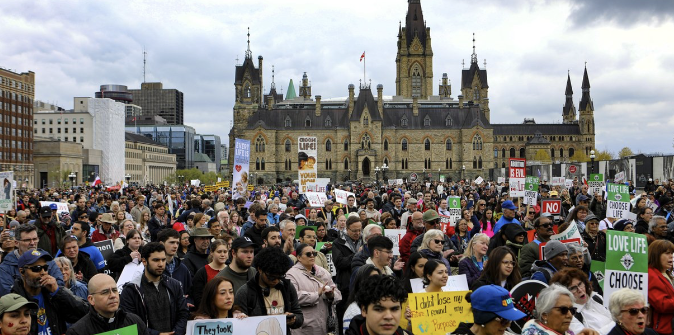 Thousands rally at Canada’s National March for Life in Ottawa – #Catholic – It took almost 25 minutes for a crowd that organizers said was in the thousands to inch its way from Parliament Hill down Wellington Street to Elgin Street during the National March for Life in Ottawa.Members of every ethnic background, young and elderly, priests, families and church groups carried pro-life signs and walked the streets of the Canadian capital to press for an end to abortion and euthanasia in Canada.The day began with liturgies celebrated at Notre Dame Cathedral, St. Patrick’s Basilica, and St. Clement. Ottawa-Cornwall Archbishop Marcel Damphousse was the main celebrant at the cathedral, joined by papal nuncio Archbishop Ivan Jurkovič, Ukrainian Catholic Bishop Bryan Bayda, and some 30 priests and deacons.
 
 Pro-life signs on Parliament Hill, May 14, 2026, at Canadaʼs March for Life. Organizer Debbie Duval told the crowd “Our legislators are sitting in the House of Commons. We want them to hear us. We want them to know we’re here.” | Credit: Peter Stockland
 
 At a midday rally before the march, organizer Debbie Duval told the crowd, “We march on a Thursday, in Ottawa, because that’s when our legislators are sitting in the House of Commons. We want them to hear us. We want them to know we’re here.”Matthew Wojciechoski, Project Manager at Campaign Life Coalition (CLC), which organizes the annual event, told the crowd, “We are here to call upon the members of Parliament to enact legal protections for all human beings from conception up to natural death. To remind Parliament of four simple words, ‘Thou shalt not kill.’”The March for Life takes place in May to mark the month in 1969 when the omnibus bill that decriminalized abortion in Canada was passed.This year’s march fell on the very anniversary of the vote and adopted as its theme Jesus’ command, “Follow me.”CLC national president Jeff Gunnarson asked the crowd to pray for founder and former president Jim Hughes who is in hospital with pneumonia and “not doing well.”“Jim devoted decades of his life to the unborn and building this movement in Canada. Many of us are standing here today because of sacrifices he made long before we arrived,” Gunnarson said.The featured speaker was Aleš Primc, co-founder of the Slovenian political party Voice for Children and Families that recently forced a referendum to overturn the country’s assisted suicide law. He led pro-lifers in a series of loud “hellos” to people of all ages, from unborn children to “people with gray hair like me.”“Saying “hello” is the start of recognizing our shared humanity,” he said.
 
 Some of the crowd on Parliament Hill for the March for Life, on May 14, 2026, in Ottawa. | Credit: Peter Stockland
 
 Speaker Rebecca Kiessling, a U.S. lawyer and founder of the organization Save the 1 — a reference to the one per cent of babies conceived in rape — said she narrowly escaped “the death penalty” in the womb at two abortion clinics.Kiessling, who was conceived in rape, has dedicated her legal career to advocating for the rights of mothers whose children were similarly conceived. She lobbies for abortion bans with no exceptions for rape or incest.Born four years prior to the landmark 1973 ruling Roe v. Wade, she said she survived only because “the (existing) law in Michigan protected me.”“I did not deserve the death penalty for the crime of the man who raped my mother. My mother chose abortion. I wasn’t lucky: I was protected. The law matters.”Conservative MP Arnold Viersen brought his two toddler children to the stage with him, one of them amusing the crowd by peeking through the railing and jumping around loudly enough to be heard over the public address system.The Parliament Hill speeches and the march through Ottawa are the centrepoint of four days of events, from a candlelight vigil the night before to pray and remember babies lost to abortion, a banquet Thursday evening, and a youth summit on Friday.Gunnarson summed up why the march continues each year. “Sometimes this work can feel difficult, sometimes we feel that no progress is being made, but then we gather here and we remember that truth does not expire, love does not quit, and courage inspires courage.”Pro-life supporters march in British ColumbiaAcross the country, ihundreds also gathered at the annual March for Life in Victoria, British Columbiaʼs capital city, where participants marched through downtown streets carrying pro-life signs and banners before rallying at the legislature to hear speakers, including Vancouver Archbishop Richard Smith.
 
 Hundreds gather at the British Columbia Legislature on May 14, 2026, for the Victoria March for Life. | Courtesy of the Diocese of Victoria
 
 The Victoria event drew families, clergy, students, and supporters from across the province for speeches, prayer, and music focused on the protection of unborn life and care for vulnerable people. Organizers also highlighted concerns surrounding euthanasia and assisted suicide.In his homily at St. Andrewʼs Cathedral in Victoria, Smith acknowledged that many pro-life advocates can feel discouraged by what he described as “a powerful juggernaut moving forward and expanding in a manner that appears irresistible,” pointing to abortion and the expansion of euthanasia in Canada.But he urged participants not to lose hope, saying, “God is at work, God is on the move, and God is an unstoppable force. His saving will simply cannot be thwarted by human iniquity.”“This is why we march,” he said. “It is incumbent upon all of us to look for any and every opportunity to witness to the truth of God’s own love for life.”
 
 Vancouverʼs Archbishop Richard Smith speaks in front of the legislature at the Victoria March for Life on May 14,2026. | Photo courtesy of the Diocese of Victoria
 
 Speaking later in front of the B.C. Legislature, Smith said the annual March for Life was part of a broader effort to build “a culture of life” through speaking, celebrating, and serving.“Our march is a very peaceful event, and a great occasion for us to witness to the beauty of all life,” he said, adding that every human being is “willed, loved and necessary.”He also said society needs “radically transformed human relationships, defined no longer by an extreme individualism and a false notion of freedom, but by a self-giving love that welcomes the other as gift.”Several other March for Life events are also scheduled across Canada later this month and into June.The Toronto March for Life will take place Saturday, May 23 at 11 a.m. at Queen’s Park North in Toronto. Organizers say a prayer service will be held beforehand at 9:30 a.m., along with workshops and educational events following the march.The Halifax March for Life in Nova Scotia is scheduled for Saturday, May 30 at 1 p.m. at St. Maryʼs Cathedral Basilica in Halifax.The Prince Edward Island March for Life will be held Saturday, June 6 at 2 p.m. at Central Christian Church in Charlottetown.The Catholic Register with B.C. Catholic filesThis article was orignally published by the B.C. Catholic and is reprinted here, with adaptations, with permission.&nbsp;