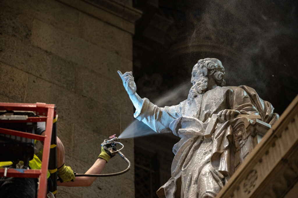Major restoration in Minneapolis aims to renew ‘every square inch’ of country’s oldest basilica #Catholic If you want to clean more-than-century-old marble statues of the apostles, you don’t simply use soap and water. Rather, you must spray the figures with a “specialized conservation material” that subsequently dries into a “latex-like layer,” which is then “carefully peeled away,” thus preserving the statue’s original finish. The process “is labor intensive and takes significant time,” according to staff at the Basilica of Saint Mary, a towering and historic minor basilica in downtown Minneapolis. The massive church, which was dedicated in 1915 and became the first basilica in the United States when it was designated as such by Pope Pius XI in 1926, has been undergoing a major restoration project since 2025. 
 
 A specialty cleaning material is sprayed on a statue of St. Peter at the Basilica of Saint Mary in Minneapolis in an undated photo. | Credit: Ken Fournelle/Courtesy of the Basilica of Saint Mary
 
 Built in the Beaux-Arts style — what was at the time a popular architectural form in the United States — the co-cathedral boasts a towering flèche-topped central dome and an 82-foot-high barrel vault. Among its many adornments include the statues of the apostles, which were carved in Italy as half-scale replicas of statues at the Archbasilica of St. John Lateran, the cathedral of the pope in Rome. Church’s roots stretch back to 1860sOn its website, the basilica says its roots can be traced to 1868, when a simple “shed church” was constructed in Minneapolis. Years later another, more substantial Gothic Revival edifice was built, but burgeoning development in the neighborhood eventually pushed the parish to relocate to its present location on Hennepin Avenue. The cornerstone of the current structure was laid in 1908. The church, designated a pro-cathedral, celebrated its first Mass in 1914; it was dedicated the following year. It was still being worked on when the U.S. entered World War I in 1917. 
 
 An original print of the basilica, drafted by architect Emmanuel Louis Masqueray, hangs in the church’s undercroft. | Credit: Courtesy of the Basilica of Saint Mary
 
 In 1926, Pius XI raised the pro-cathedral to the rank of minor basilica, after which it took on its present name. It would enjoy a vibrant parish life in the following decades, though the construction of adjacent freeways in the 1960s “took a heavy toll” on the building. The 1980s and 1990s saw parishioners spearheading efforts at ongoing restoration. The latest restoration campaign, titled “Restoring Beauty, Inspiring Hope,” has aimed to raise a total of about  million in funding. Among the project’s goals are masonry repairs, roof repairs, pew restorations with new kneelers, plaster restoration, and numerous other projects. 
 
 Workers in an undated photograph clean a limestone surface in an ambulatory of the Basilica of Saint Mary in Minneapolis. | Credit: Photo courtesy of the Basilica of Saint Mary
 
 Johan van Parys, who has served as the basilica’s director of liturgy and the sacred arts since 1995, told EWTN News that the basilica has needed repairs almost from its inception. “Even from the beginning, the building had issues with moisture intrusion,” he said. The architect who designed the church, Emmanuel Louis Masqueray, was French, and he “didn’t completely understand the challenges of Minnesota summers and winters.” “He designed flat roofs over part of the building,” van Parys said. He jokingly described flat roofs as “the bane of our existence” due to their tendency to hold water. In existing photographs of the church taken in 1914, van Parys said, water damage is already visible. “We’ve had to do work on the building ever since,” he said. The church underwent a “somewhat major” restoration in the 1950s, van Parys said, during which for unknown reasons workers painted over intricate stenciling within coffers and other parts of the structure. Along with those details, van Parys said, the restoration effort is “bringing back the original look of the basilica.” The effort was formally launched in 2019 with a master plan for the entire church campus, but the COVID-19 pandemic the next year set the project back. The process resumed after a few years, and the restoration work itself formally began in 2025. 
 
 Scaffolding towers above the nave of the Basilica of Saint Mary in Minneapolis in an undated photograph. | Credit: Ken Fournelle/Courtesy of the Basilica of Saint Mary
 
 Van Parys said the basilica is being restored both inside and out from top to the bottom, including the plaster ceiling, which has suffered damage over the years and has to be replastered in parts. Work is also being done on the church’s extensive stained-glass window arrangements. Such windows are generally held in place with a lead matrix, but over time the weight of the glass can weaken the metal frame, leading the glass to bulge outward. A stained-glass specialist, however, told the restoration crew that the window fixtures were in “great condition,” meaning considerable amounts of work could be avoided. Some of the windows were still in need of repair, however, and were sent to a specialist in Newark, New Jersey. Limestone throughout the building is also being restored, van Parys said. The visible stone throughout the building is bolstered by several inches of reinforced concrete and bricks; moisture often makes its way through this sandwiching of materials, leading to a buildup of salt crystals on the stone, what is known as “efflorescence.” Removing this blemish beautifies the facade of the stone and also protects it from degradation. Crews use a spray-and-peel chemical similar to the process used on the statues of the apostles. 
 
 A century’s worth of visible soot and grime contrasts with a restored limestone surface in an undated photograph in the Basilica of Saint Mary, Minneapolis. | Credit: Photo courtesy of the Basilica of Saint Mary
 
 The restoration crews also removed the basilica’s pews in order to have them restored with cleaning, sanding, and shellac finishing.“We opted to restore the original 1914 pews,” van Parys said. “One of our principles in terms of restoration is that we don’t want to over-restore. We didn’t want it to be a new church. People have worshipped in here since 1914. We want this presence of prayer and generations before us to remain.”“So rather than have new pews we decided to restore the old ones,” he said. “In doing so we discovered that the people who built the pews in 1914 signed them. So we have the names of all the people who worked on the pews.”
 
 Workmen in an undated photo remove pews from the Basilica of Saint Mary in Minneapolis as part of the restoration of the church. | Credit: Ken Fournelle/Courtesy of the Basilica of Saint Mary
 
 Upon removing the pews, the work crews discovered that the flooring of the nave was not level. “One option was to put shims under all the pews,” van Parys said. “But that would have been a huge operation.” Since crews were already removing the wood flooring to restore it, they also removed part of the old concrete subfloor and re-leveled it.
 
 A worker at Fresh Air Finishers in Saint Paul, Minnesota, restores a pew from the Basilica of Saint Mary in an undated photograph. | Credit: Ken Fournelle/Courtesy of the Basilica of Saint Mary
 
 Numerous other restoration projects are ongoing, van Parys said, including restoring the church’s bronze doors, which were installed after it was designated a basilica. The church’s rector at the time, Monsignor James Reardon, had traveled to Rome and observed that the basilicas there had bronze doors. “He decided we needed bronze doors as well,” van Parys said. 
 
 Archbishop Bernard Hebda blesses and seals bronze doors at the Basilica of Saint Mary ahead of restoration of the century-old features of the historic church, April 5, 2026. | Credit: Photo courtesy of the Basilica of Saint Mary
 
 Crews are aiming to be done with the massive project by Palm Sunday 2027. At the moment the parish holds Masses in the building’s undercroft beneath the structure. “Every week at Mass, I tell people, for instance, ‘Last Sunday was Week 35, which means we have 34 weeks to go,’” van Parys said with a laugh. He said the work is “quite expedited” and progressing quickly. Ultimately the effort is meant not just to restore the church but to develop a “manual of preservation” for future generations to help protect it. “Our goal is to restore and to also make sure that everything is cared for in the best possible way, to extend the lifespan of the basilica as long as possible before another restoration is necessary,” he said. He said the entire project is being conducted “not only with liturgical principles but also historical preservation principles.”“It is really comprehensive,” he said. “Every square inch of the basilica will be restored.”