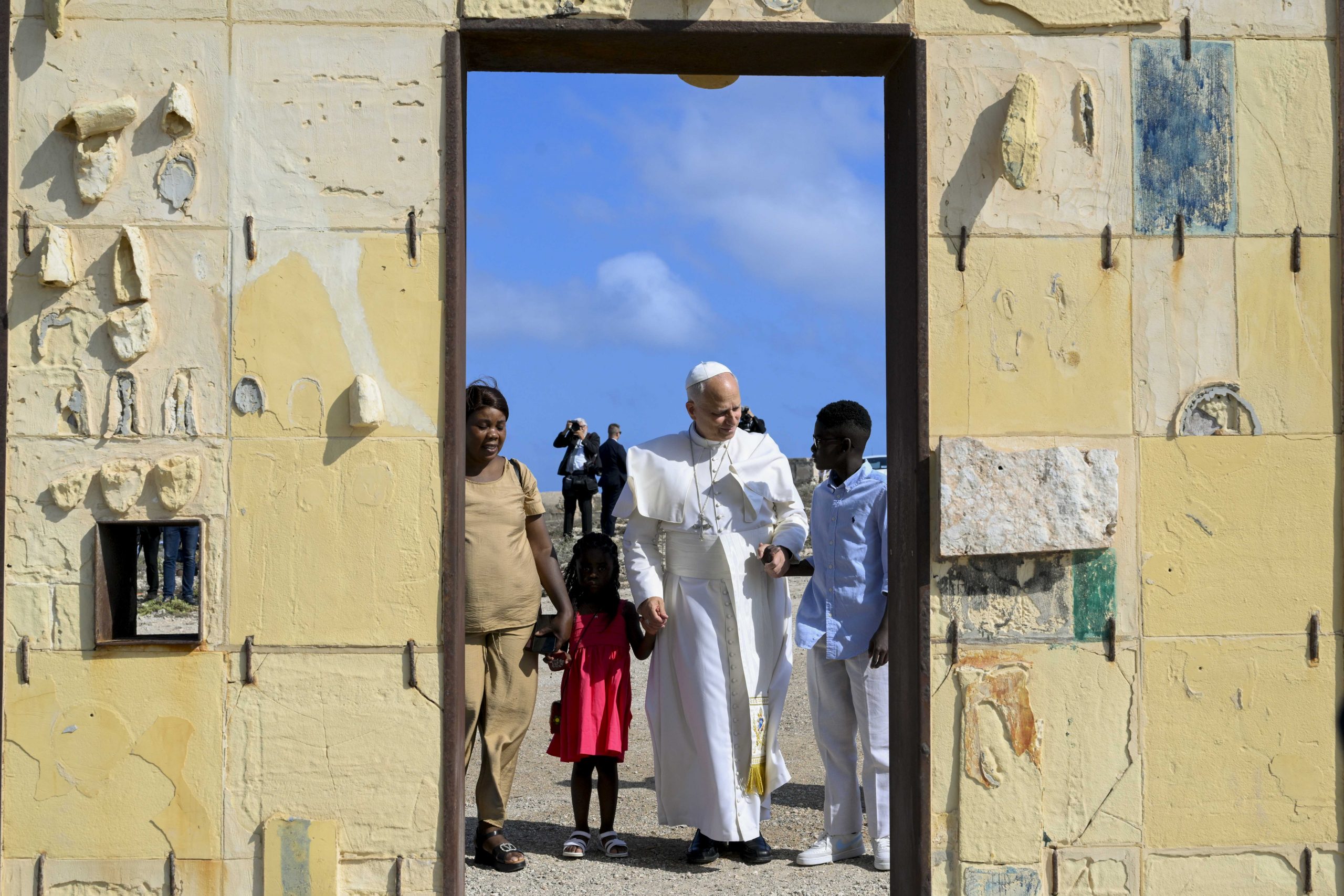 Pope Leo XIV: Migrants lost at sea are victims of choices made and unmade – #Catholic – Pope Leo XIV celebrated Mass Saturday on the island of Lampedusa, warning that migrants who have died crossing the Mediterranean are “victims both of decisions that were made and of decisions that were not made.”In his homily at the Arena sports field July 4, the pope cited the Gospel parable of the Good Samaritan, saying residents of Lampedusa had seen “thousands of human beings fallen into the hands of robbers who have taken everything from them, beat them brutally and walked away, leaving them half-dead.”“The sea has claimed the lives of others — those who did not manage to reach their hoped-for destination,” he said. “Yet we feel their presence, which challenges us no less than that of those who have landed in need of attention and aid.”The pope arrived at the sports field in a Fiat Nuova Campagnola convertible, the same vehicle Pope Francis used during his July 8, 2013, visit to Lampedusa. The crowd greeted him with songs, waving arms, and yellow-and-white caps against the backdrop of the island’s sea and sky.Before the liturgy, Lampedusa’s mayor presented the pope with a model of the island’s lighthouse. Pope Leo recalled Pope Francis’ closeness to the people of Lampedusa and said he had come not primarily to give speeches but to celebrate the Eucharist, the supreme sign of Christ’s presence.The pope’s homily repeatedly returned to the theme of love — a love made concrete in compassion, hospitality, and the willingness to draw near to those in need.“The Gospel resounds where peoples meet, people welcome one another, their lives intertwine and different cultures engage in dialogue,” he said. “It falls silent, however, when each person makes him or herself an island, avoiding contact and cutting off exchange.”Citing the parable of the Good Samaritan, the pope said the encounter with those stripped of everything calls Christians “to be close to them.”“This is the heart of the Gospel parable: we become neighbors by acting as neighbors,” he said.Pope Leo thanked the people of Lampedusa for what he called the “miracle of compassion,” including the volunteers, organizations in Forum Lampedusa Solidale, civil authorities, the Coast Guard, local administrations, deacons, priests, religious sisters, doctors, psychologists, educators, security forces, and all those who serve migrants on the island.“I greet the migrants who are here,” he added. “They themselves have not only received solidarity but have often shown it on their journey, as the poor helping the poorest.”But the pope also warned against indifference, corruption, fear, prejudice, and policies that fail to respond to the scale of the crisis.“Indifference to the common good and corruption in their countries of origin; a global economic system that generates poverty and exclusion; fear that fuels prejudice and contempt; the belief that such problems do not concern us; the criminal calculations of those who profit from the suffering of others; the slow and difficult transition from mere emergency management to the development of comprehensive and shared policies — all are present-day echoes of the haste to ‘pass by’ in the Gospel narrative,” he said.Pope Leo also said religious belonging must never be used to exclude or discriminate.“It is time to recognize and affirm that religious affiliation must never become a reason for discrimination, as if faith had boundaries rather than being a universal call to salvation,” he said. “There is no love of God without love of neighbor, and there is no neighbor if I do not draw near.”From Lampedusa, which lies between Sicily and North Africa and has become a symbol of the migration crisis in the Mediterranean, the pope turned his attention to Europe.“From this far-flung corner of Europe on the Mediterranean Sea, one can more clearly perceive the momentous challenge that the phenomenon of migration poses to European societies,” he said.Europe, he continued, has “a unique potential” and therefore “a corresponding responsibility” to address migration in a comprehensive way — integrating immediate relief into “a long-term strategic plan capable of receiving, protecting, supporting and integrating migrants,” while also assisting developing countries so that “no one is forced to emigrate.”The pope said the task belongs not only to public institutions but also to civil society and the Church.Speaking directly to the people of Lampedusa, he also noted that tourism on the island can risk creating an “invisible wall” between vacationers and migrants who have survived shipwrecks.“Have the courage to think differently,” he said, urging residents to help visitors become “more humane” through contact with the island’s charity and history.“There is authentic rest when the meaning of life is rediscovered, and true well-being when the economy is just and fraternal,” the pope said. “In such an economy, care for creation and social friendship come together in a synthesis that humanity is seeking today.”At the close of his homily, Pope Leo referred to the image of Our Lady of Safe Harbor, patroness of Lampedusa, placed near the altar.“In God we all have a safe haven, and every Christian community is called to be a reflection of it on earth,” he said. He ended with the traditional local greeting: “O’scià!”Before the Mass, the pope visited the cemetery of Lampedusa, where he placed flowers on the graves of migrants, pausing especially at the graves of children. The moment was marked by silence and strong wind.He then went to the Porta d’Europa, the “Gateway to Europe” monument, where he briefly met a migrant family. A child gave him a soccer ball and read him a note.“Dear pope, I am super excited to meet you. Ten years ago my story began here in Lampedusa. I was alone and had lost everything, especially my mother,” the child wrote.The child said he had stopped crying only after someone gave him a ball made of paper.“From that day, the ball has remained in my heart, and I have never stopped playing,” he wrote. “Now I hope that this ball I am giving you can reach another child and make him happy, just like me.”The pope then moved toward the sea to pray alone. The wind swept away his white zucchetto, which fell into the water as he prayed near the sea.Before heading to the Arena sports field, Pope Leo visited Molo Favaloro, where he blessed a plaque dedicating the dock to Pope Francis. There he greeted migrants accompanied by the Red Cross, as well as religious sisters who are among the first to welcome migrants arriving on the island.The visit came a day after the U.S.-born Pope Leo, accepting the Liberty Medal awarded by the National Constitutional Center in Philadelphia, recalled how his native land had opened its doors to waves of immigrants, allowing them and their children to help build the nation’s future. The pope has been critical of Trump administration’s policies on immigration and the coincidence of his visit to Lampedusa with America’s 250th anniversary has been widely noted there.This story was first published in two parts by ACI Stampa, the Italian-language sister service of EWTN News. It has been translated and adapted by EWTN News English.Sources used: ACI Stampa Mass report and official English homily text . Pope Leo XIV: Migrants lost at sea are victims of choices made and unmade – #Catholic – Pope Leo XIV celebrated Mass Saturday on the island of Lampedusa, warning that migrants who have died crossing the Mediterranean are “victims both of decisions that were made and of decisions that were not made.”In his homily at the Arena sports field July 4, the pope cited the Gospel parable of the Good Samaritan, saying residents of Lampedusa had seen “thousands of human beings fallen into the hands of robbers who have taken everything from them, beat them brutally and walked away, leaving them half-dead.”“The sea has claimed the lives of others — those who did not manage to reach their hoped-for destination,” he said. “Yet we feel their presence, which challenges us no less than that of those who have landed in need of attention and aid.”The pope arrived at the sports field in a Fiat Nuova Campagnola convertible, the same vehicle Pope Francis used during his July 8, 2013, visit to Lampedusa. The crowd greeted him with songs, waving arms, and yellow-and-white caps against the backdrop of the island’s sea and sky.Before the liturgy, Lampedusa’s mayor presented the pope with a model of the island’s lighthouse. Pope Leo recalled Pope Francis’ closeness to the people of Lampedusa and said he had come not primarily to give speeches but to celebrate the Eucharist, the supreme sign of Christ’s presence.The pope’s homily repeatedly returned to the theme of love — a love made concrete in compassion, hospitality, and the willingness to draw near to those in need.“The Gospel resounds where peoples meet, people welcome one another, their lives intertwine and different cultures engage in dialogue,” he said. “It falls silent, however, when each person makes him or herself an island, avoiding contact and cutting off exchange.”Citing the parable of the Good Samaritan, the pope said the encounter with those stripped of everything calls Christians “to be close to them.”“This is the heart of the Gospel parable: we become neighbors by acting as neighbors,” he said.Pope Leo thanked the people of Lampedusa for what he called the “miracle of compassion,” including the volunteers, organizations in Forum Lampedusa Solidale, civil authorities, the Coast Guard, local administrations, deacons, priests, religious sisters, doctors, psychologists, educators, security forces, and all those who serve migrants on the island.“I greet the migrants who are here,” he added. “They themselves have not only received solidarity but have often shown it on their journey, as the poor helping the poorest.”But the pope also warned against indifference, corruption, fear, prejudice, and policies that fail to respond to the scale of the crisis.“Indifference to the common good and corruption in their countries of origin; a global economic system that generates poverty and exclusion; fear that fuels prejudice and contempt; the belief that such problems do not concern us; the criminal calculations of those who profit from the suffering of others; the slow and difficult transition from mere emergency management to the development of comprehensive and shared policies — all are present-day echoes of the haste to ‘pass by’ in the Gospel narrative,” he said.Pope Leo also said religious belonging must never be used to exclude or discriminate.“It is time to recognize and affirm that religious affiliation must never become a reason for discrimination, as if faith had boundaries rather than being a universal call to salvation,” he said. “There is no love of God without love of neighbor, and there is no neighbor if I do not draw near.”From Lampedusa, which lies between Sicily and North Africa and has become a symbol of the migration crisis in the Mediterranean, the pope turned his attention to Europe.“From this far-flung corner of Europe on the Mediterranean Sea, one can more clearly perceive the momentous challenge that the phenomenon of migration poses to European societies,” he said.Europe, he continued, has “a unique potential” and therefore “a corresponding responsibility” to address migration in a comprehensive way — integrating immediate relief into “a long-term strategic plan capable of receiving, protecting, supporting and integrating migrants,” while also assisting developing countries so that “no one is forced to emigrate.”The pope said the task belongs not only to public institutions but also to civil society and the Church.Speaking directly to the people of Lampedusa, he also noted that tourism on the island can risk creating an “invisible wall” between vacationers and migrants who have survived shipwrecks.“Have the courage to think differently,” he said, urging residents to help visitors become “more humane” through contact with the island’s charity and history.“There is authentic rest when the meaning of life is rediscovered, and true well-being when the economy is just and fraternal,” the pope said. “In such an economy, care for creation and social friendship come together in a synthesis that humanity is seeking today.”At the close of his homily, Pope Leo referred to the image of Our Lady of Safe Harbor, patroness of Lampedusa, placed near the altar.“In God we all have a safe haven, and every Christian community is called to be a reflection of it on earth,” he said. He ended with the traditional local greeting: “O’scià!”Before the Mass, the pope visited the cemetery of Lampedusa, where he placed flowers on the graves of migrants, pausing especially at the graves of children. The moment was marked by silence and strong wind.He then went to the Porta d’Europa, the “Gateway to Europe” monument, where he briefly met a migrant family. A child gave him a soccer ball and read him a note.“Dear pope, I am super excited to meet you. Ten years ago my story began here in Lampedusa. I was alone and had lost everything, especially my mother,” the child wrote.The child said he had stopped crying only after someone gave him a ball made of paper.“From that day, the ball has remained in my heart, and I have never stopped playing,” he wrote. “Now I hope that this ball I am giving you can reach another child and make him happy, just like me.”The pope then moved toward the sea to pray alone. The wind swept away his white zucchetto, which fell into the water as he prayed near the sea.Before heading to the Arena sports field, Pope Leo visited Molo Favaloro, where he blessed a plaque dedicating the dock to Pope Francis. There he greeted migrants accompanied by the Red Cross, as well as religious sisters who are among the first to welcome migrants arriving on the island.The visit came a day after the U.S.-born Pope Leo, accepting the Liberty Medal awarded by the National Constitutional Center in Philadelphia, recalled how his native land had opened its doors to waves of immigrants, allowing them and their children to help build the nation’s future. The pope has been critical of Trump administration’s policies on immigration and the coincidence of his visit to Lampedusa with America’s 250th anniversary has been widely noted there.This story was first published in two parts by ACI Stampa, the Italian-language sister service of EWTN News. It has been translated and adapted by EWTN News English.Sources used: ACI Stampa Mass report and official English homily text .