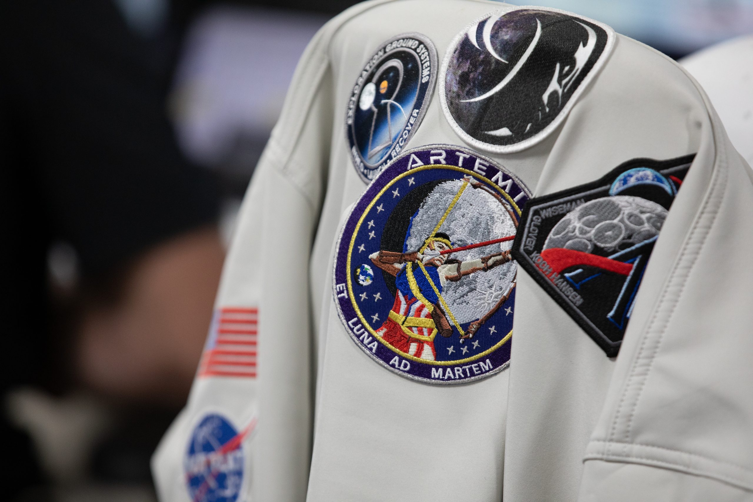 Artemis Mission Patches – A NASA jacket containing Artemis I and II mission patches, along with other NASA patches hangs on the back of a chair on Thursday, Aug. 6, 2026, inside Firing Room 1 of the Rocco A. Petrone Launch Control Center at NASA’s Kennedy Space Center in Florida during a terminal countdown simulation for the Artemis III mission.