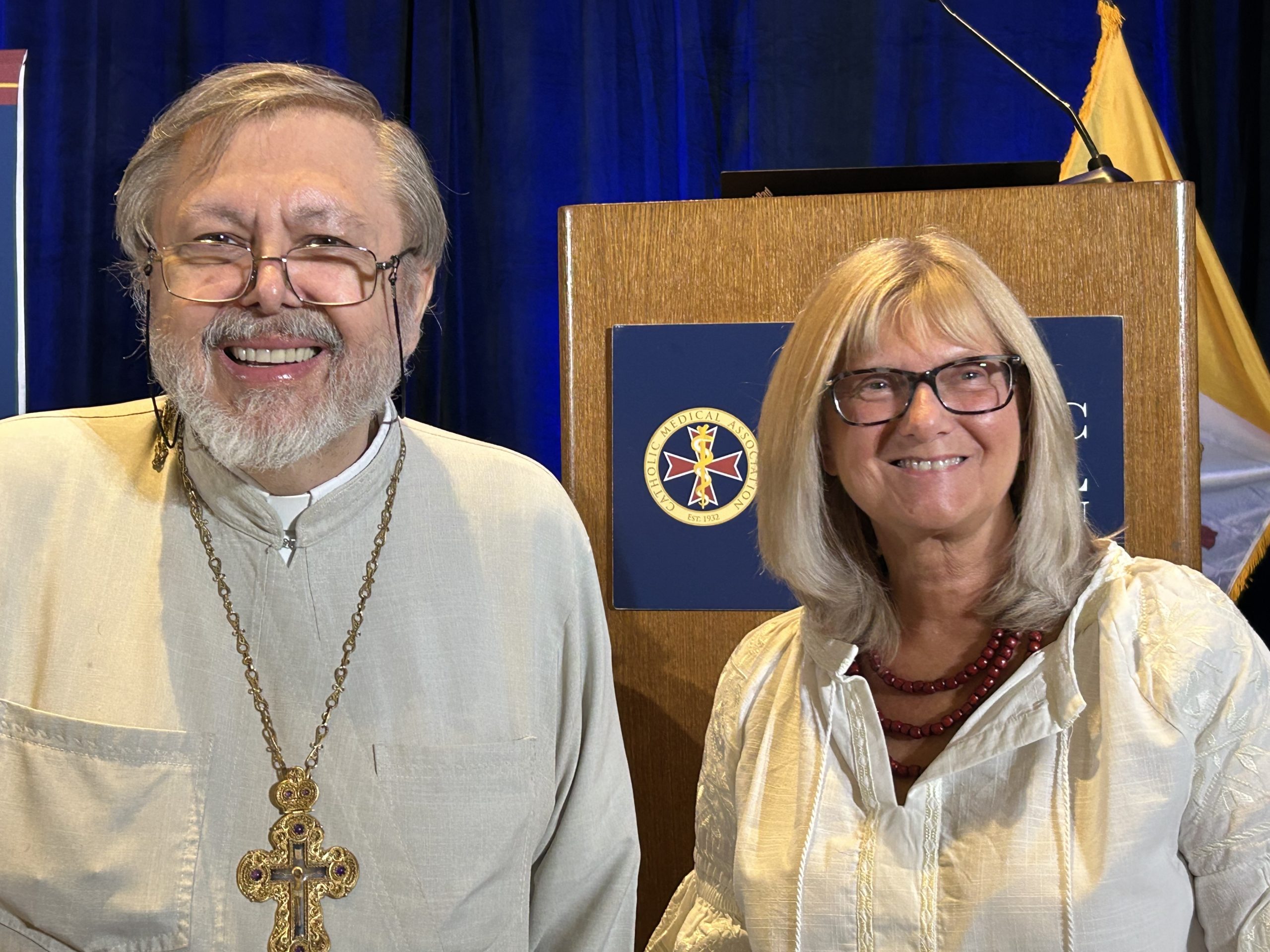 Catholic doctors say both Eastern and Western spirituality are required to heal the whole person – #Catholic – PHOENIX — For the first time in its nearly 100-year history, the Catholic Medical Association is focusing on how the Eastern Catholic Church’s emphasis on mystery, united with the Western Church’s emphasis on reason, can give a more comprehensive view of human identity and help Western medicine promote human flourishing.The group’s 95th annual educational conference, held in Phoenix Sept. 10–12, emphasized the early Church Fathers, whose influence was strongest in the East, in order to “promote a more comprehensive view and more respect for the mysteries of human health and disease,” said conference chair Dr. Mary Keen-Kirchoff.“We’re embodied spirits, not just physical bodies,” she said at the opening. Healing, she added, “is a return to humanity’s original creation in the image and likeness of God.”The conference theme was “Mysteries and Miracles: Restoring the Practice of Medicine to Heal the Whole Person.” Setting the tone, Father Andriy Chirovsky, a theologian and priest of the Ukrainian Greco-Catholic Church, an Eastern Catholic Church in full communion with Rome, and psychiatrist Dr. Donna C. Dobrowolsky shared the first plenary.They moved between theology and clinical practice, saying they hoped to help medical professionals recover a holistic understanding of “the whole person, because thatʼs who all of us care about.” Theology without clinical reality stays abstract, they said; clinical work without a complete Christian anthropology becomes fragmented.“If the human person is misunderstood, then healing will also be misunderstood and therefore less effective,” Chirovsky said. “Healing requires a true anthropology.”He quoted Pope Leo XIV’s encyclical Magnifica Humanitas, in which the pontiff wrote: “We Christians lift our eyes to the Incarnate God, knowing that it is ‘only the mystery of the Word made flesh that the mystery of humanity truly becomes clear.’”Why the East, and why now?Chirovsky cited St. John Paul II’s 1995 encyclical Ut Unum Sint (That They May Be One), in which the pope, referring to the Eastern and Western Catholic churches, wrote that “the Church must breathe with her two lungs!”Dobrowolsky noted that what the West calls sacraments, the East calls mysteries: rites “not fully comprehensible by human reason, but revealed by God.”Chirovsky said Eastern spirituality and practice “preserve certain habits of thought that are especially needed at this moment in history.”He was not arguing against the West, he said. Any strength can become distorted when it loses its complement. The East offers “a needed medicine for some of the pathologies of modern culture,” especially the idea that a person is the center of the universe, “self-defining,” and “the ground of truth.”“We require revelation to understand our own selves,” he said.“If the person is not self-explaining,” Dobrowolsky said, medicine has to be careful because lab values and symptom clusters aren’t enough to explain a person. They’re important, but they don’t tell us everything about who a human person is.”The Catholic Church needs both the East and the West in the same way a healthy person must think with both hemispheres of the brain, the priest said, quoting neuroscientist Iain McGilchrist’s book “The Master and His Emissary: The Divided Brain and the Making of the Western World.”In his book, McGilchrist notes that the left side of the brain is analytical and narrow, while the right side focuses more on the big picture, and pathology results when the two sides don’t work together and one side dominates.Chirovsky compared modern medicine’s laser focus on the analytical and quantifiable, using hyperspecialization in the medical field as an example, to a pathology with too much dependence on the left brain.“The analytic mode is powerful, but when it dominates unchecked, the person becomes legible as data but less visible as mystery and as a person,” he said.“Any practice of medicine that loses sight of the whole person as revealed in the incarnate Son of God is going to run into lots of trouble,” he added. “Modern medicine is doing exactly that.”Dobrowolsky agreed, adding that “in medicine, that imbalance isn’t theoretical, we see it every day.”Seeing the human being as mystery does not mean the person is unintelligible, she said. “We’re saying this human person is not exhausted by reductionist accounts. And that the deepest truth of the human person is disclosed in relation to Christ.”“If a person is reduced to a collection of functions, risks, and measurable outputs, their care becomes reduced as well,” she continued, saying that while practitioners may “retain technical brilliance … the patient may begin to disappear beneath the technique.”Indeed, the conference’s breakout sessions touched upon the necessity for a Christian anthropology informed by a Church “breathing with both lungs," with talks titled “Healing Is Not the Same as Curing: Patristic Anthropology and the Limits of Modern Medicine,” “The Neglected Soul: Ancient Monastic Teachings on Depression in the Modern World,” and “Psychedelics, AI, Spirituality, and More: Ancient Wisdom for Reenchanting Medicine.”“My prayer before the conference was that all attendees receive abundant graces of understanding and hope for the future,” Keen-Kirchoff told EWTN News. “I am so grateful that the Holy Spirit was so present … and trust that attendees are more in tune with who we are in Christ and who we are to become in Christ.”
Bishop James Conley, center, receives the 2026 Evangelium Vitae award. He stands with Mario Dickerson, CMA executive director, left, and Dr. Mary Keen-Kirchoff, CMA conference chair, on Sept. 10, 2026. | Credit: Photo courtesy of Catholic Medical Association
Bishop James D. Conley of the Diocese of Lincoln, Nebraska, won the CMA’s annual Evangelium Vitae award for his pastoral efforts surrounding mental health. In May 2024, Conley published a pastoral letter titled “A Future with Hope,” concerning the Catholic response to mental health struggles. The honor sits close to the conference’s theme: care that views the person as a whole, in the mystery of body and spirit. Catholic doctors say both Eastern and Western spirituality are required to heal the whole person – #Catholic – PHOENIX — For the first time in its nearly 100-year history, the Catholic Medical Association is focusing on how the Eastern Catholic Church’s emphasis on mystery, united with the Western Church’s emphasis on reason, can give a more comprehensive view of human identity and help Western medicine promote human flourishing.The group’s 95th annual educational conference, held in Phoenix Sept. 10–12, emphasized the early Church Fathers, whose influence was strongest in the East, in order to “promote a more comprehensive view and more respect for the mysteries of human health and disease,” said conference chair Dr. Mary Keen-Kirchoff.“We’re embodied spirits, not just physical bodies,” she said at the opening. Healing, she added, “is a return to humanity’s original creation in the image and likeness of God.”The conference theme was “Mysteries and Miracles: Restoring the Practice of Medicine to Heal the Whole Person.” Setting the tone, Father Andriy Chirovsky, a theologian and priest of the Ukrainian Greco-Catholic Church, an Eastern Catholic Church in full communion with Rome, and psychiatrist Dr. Donna C. Dobrowolsky shared the first plenary.They moved between theology and clinical practice, saying they hoped to help medical professionals recover a holistic understanding of “the whole person, because thatʼs who all of us care about.” Theology without clinical reality stays abstract, they said; clinical work without a complete Christian anthropology becomes fragmented.“If the human person is misunderstood, then healing will also be misunderstood and therefore less effective,” Chirovsky said. “Healing requires a true anthropology.”He quoted Pope Leo XIV’s encyclical Magnifica Humanitas, in which the pontiff wrote: “We Christians lift our eyes to the Incarnate God, knowing that it is ‘only the mystery of the Word made flesh that the mystery of humanity truly becomes clear.’”Why the East, and why now?Chirovsky cited St. John Paul II’s 1995 encyclical Ut Unum Sint (That They May Be One), in which the pope, referring to the Eastern and Western Catholic churches, wrote that “the Church must breathe with her two lungs!”Dobrowolsky noted that what the West calls sacraments, the East calls mysteries: rites “not fully comprehensible by human reason, but revealed by God.”Chirovsky said Eastern spirituality and practice “preserve certain habits of thought that are especially needed at this moment in history.”He was not arguing against the West, he said. Any strength can become distorted when it loses its complement. The East offers “a needed medicine for some of the pathologies of modern culture,” especially the idea that a person is the center of the universe, “self-defining,” and “the ground of truth.”“We require revelation to understand our own selves,” he said.“If the person is not self-explaining,” Dobrowolsky said, medicine has to be careful because lab values and symptom clusters aren’t enough to explain a person. They’re important, but they don’t tell us everything about who a human person is.”The Catholic Church needs both the East and the West in the same way a healthy person must think with both hemispheres of the brain, the priest said, quoting neuroscientist Iain McGilchrist’s book “The Master and His Emissary: The Divided Brain and the Making of the Western World.”In his book, McGilchrist notes that the left side of the brain is analytical and narrow, while the right side focuses more on the big picture, and pathology results when the two sides don’t work together and one side dominates.Chirovsky compared modern medicine’s laser focus on the analytical and quantifiable, using hyperspecialization in the medical field as an example, to a pathology with too much dependence on the left brain.“The analytic mode is powerful, but when it dominates unchecked, the person becomes legible as data but less visible as mystery and as a person,” he said.“Any practice of medicine that loses sight of the whole person as revealed in the incarnate Son of God is going to run into lots of trouble,” he added. “Modern medicine is doing exactly that.”Dobrowolsky agreed, adding that “in medicine, that imbalance isn’t theoretical, we see it every day.”Seeing the human being as mystery does not mean the person is unintelligible, she said. “We’re saying this human person is not exhausted by reductionist accounts. And that the deepest truth of the human person is disclosed in relation to Christ.”“If a person is reduced to a collection of functions, risks, and measurable outputs, their care becomes reduced as well,” she continued, saying that while practitioners may “retain technical brilliance … the patient may begin to disappear beneath the technique.”Indeed, the conference’s breakout sessions touched upon the necessity for a Christian anthropology informed by a Church “breathing with both lungs," with talks titled “Healing Is Not the Same as Curing: Patristic Anthropology and the Limits of Modern Medicine,” “The Neglected Soul: Ancient Monastic Teachings on Depression in the Modern World,” and “Psychedelics, AI, Spirituality, and More: Ancient Wisdom for Reenchanting Medicine.”“My prayer before the conference was that all attendees receive abundant graces of understanding and hope for the future,” Keen-Kirchoff told EWTN News. “I am so grateful that the Holy Spirit was so present … and trust that attendees are more in tune with who we are in Christ and who we are to become in Christ.”
Bishop James Conley, center, receives the 2026 Evangelium Vitae award. He stands with Mario Dickerson, CMA executive director, left, and Dr. Mary Keen-Kirchoff, CMA conference chair, on Sept. 10, 2026. | Credit: Photo courtesy of Catholic Medical Association
Bishop James D. Conley of the Diocese of Lincoln, Nebraska, won the CMA’s annual Evangelium Vitae award for his pastoral efforts surrounding mental health. In May 2024, Conley published a pastoral letter titled “A Future with Hope,” concerning the Catholic response to mental health struggles. The honor sits close to the conference’s theme: care that views the person as a whole, in the mystery of body and spirit.